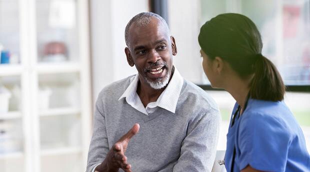 Two colleagues seated at a table engaging in conversation with a colleague standing nearby